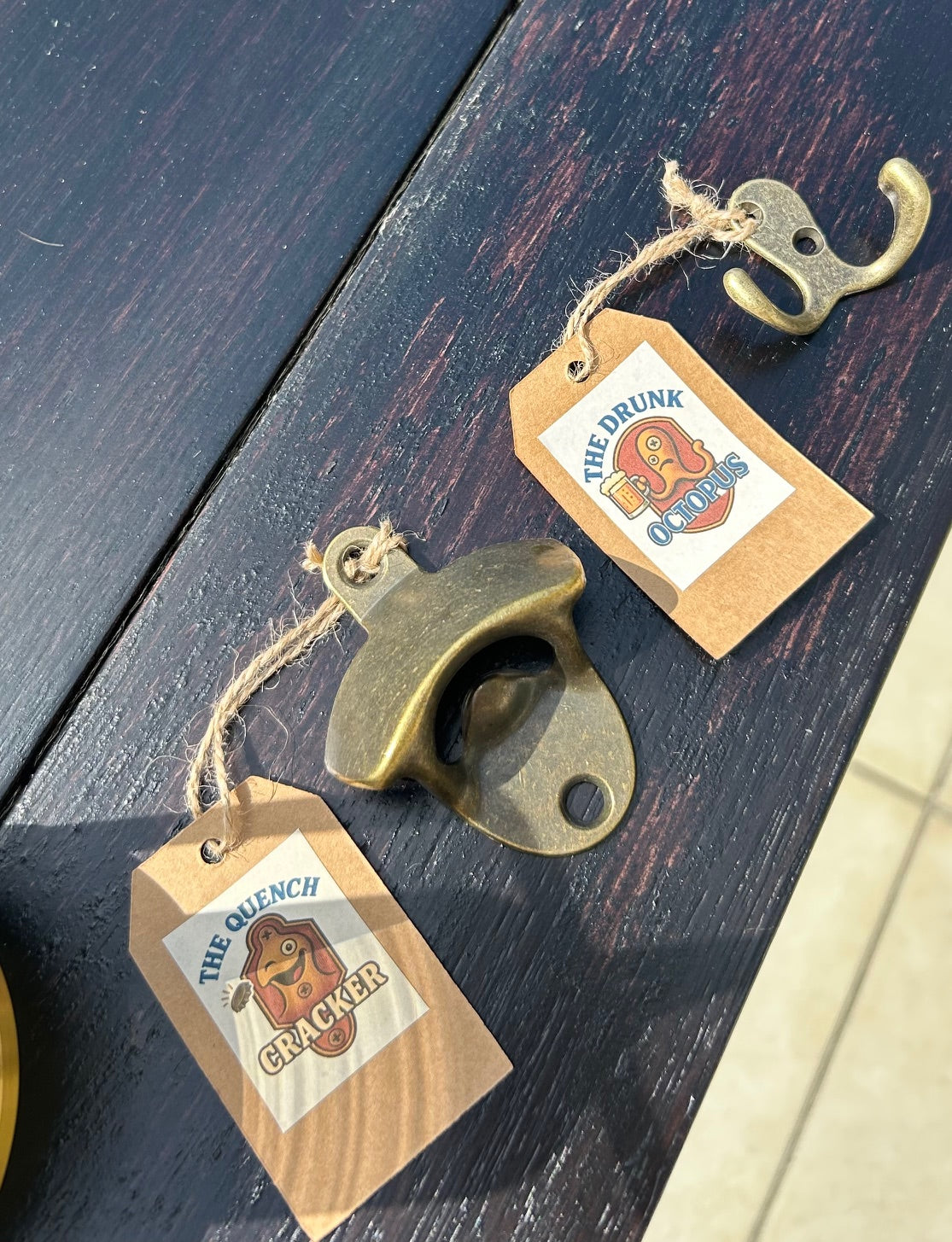 Two brass bottle openers with tags on a dark wooden surface