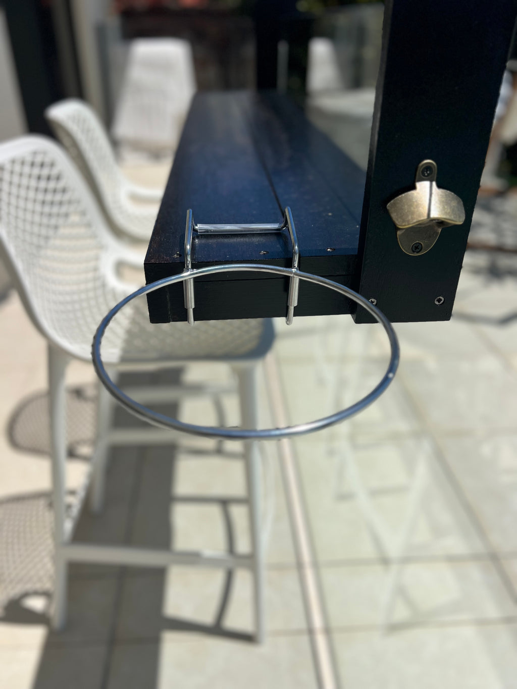 Metal hoop attached to a black rectangular object on a patio with chairs and a table in the background.