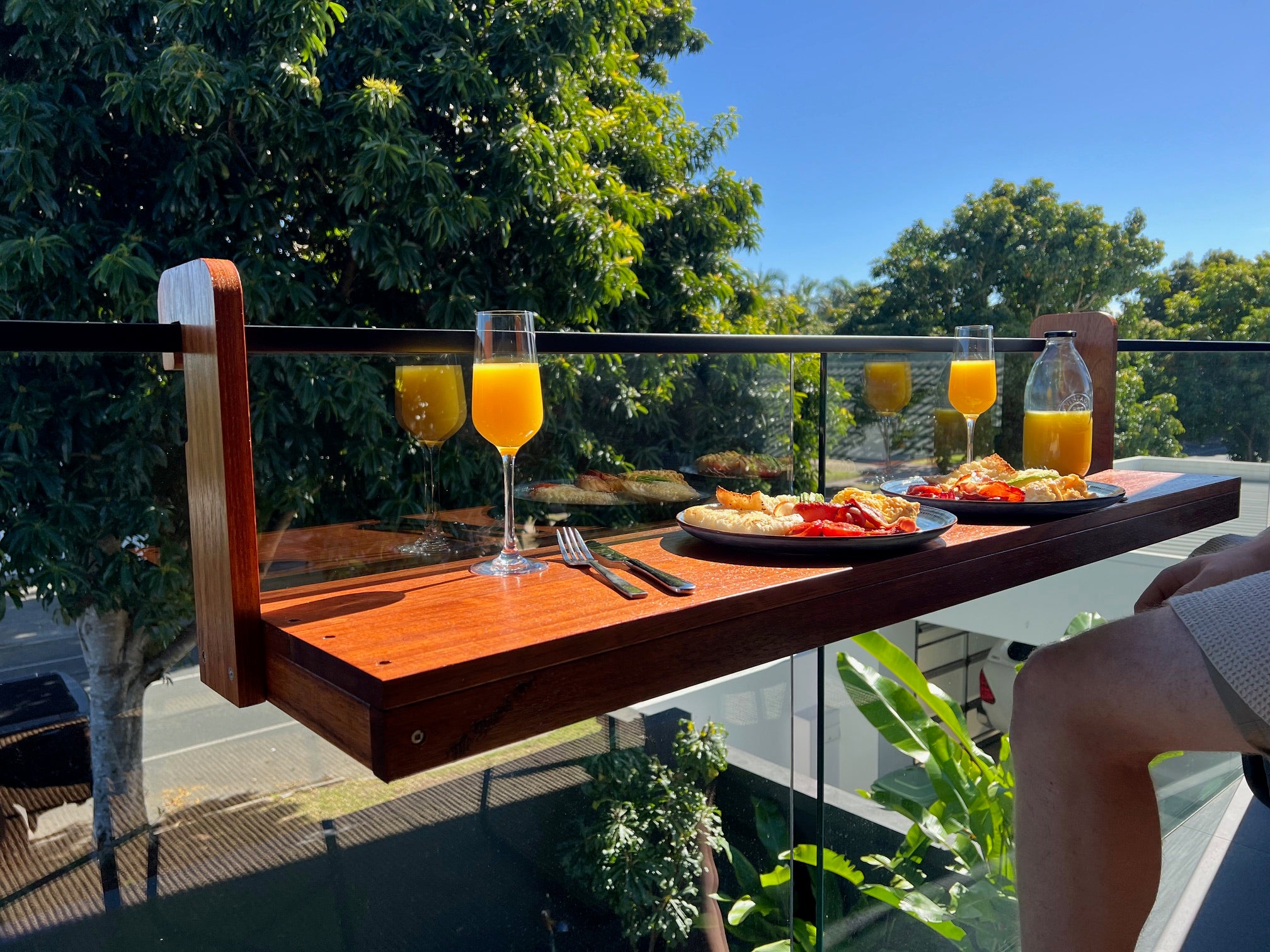 Outdoor setting with a wooden tray holding glasses of orange juice and plates of food on a balcony.